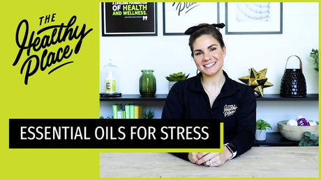 A woman in a 'Find Your Healthy Place' zip-up sits at a table with a wellness-themed background. Text overlay reads 'ESSENTIAL OILS FOR STRESS.'