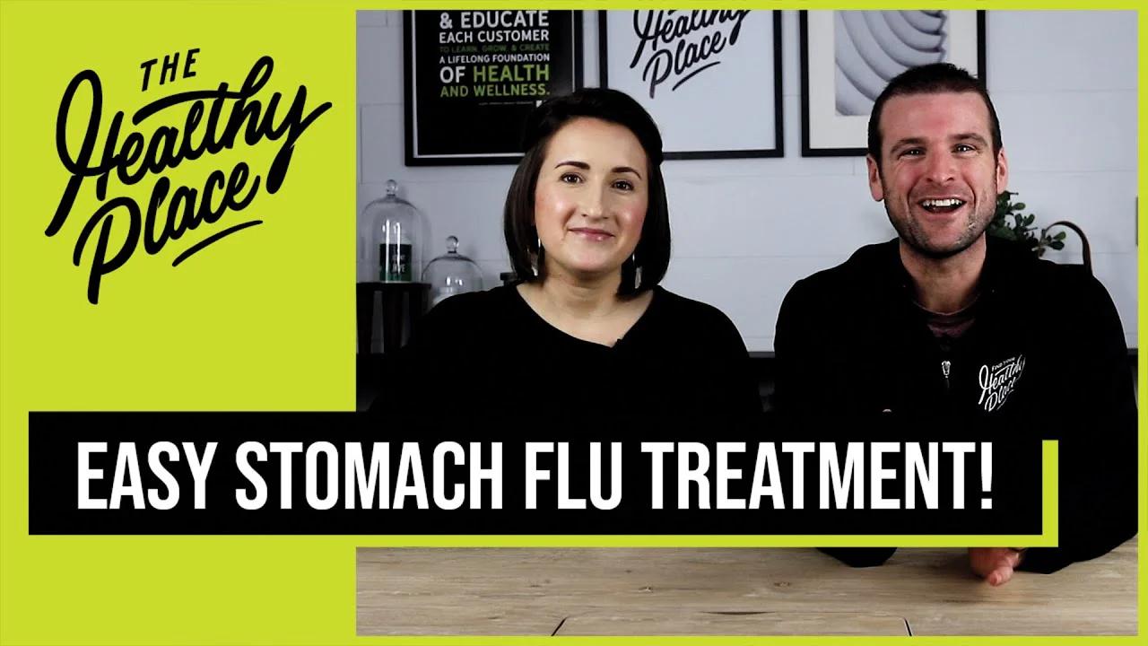 A smiling man and woman, both wearing black 'Find Your Healthy Place' branded apparel, sit together. A bold black and white text overlay reads 'EASY STOMACH FLU TREATMENT!' with 'The Healthy Place' logo on the left side.