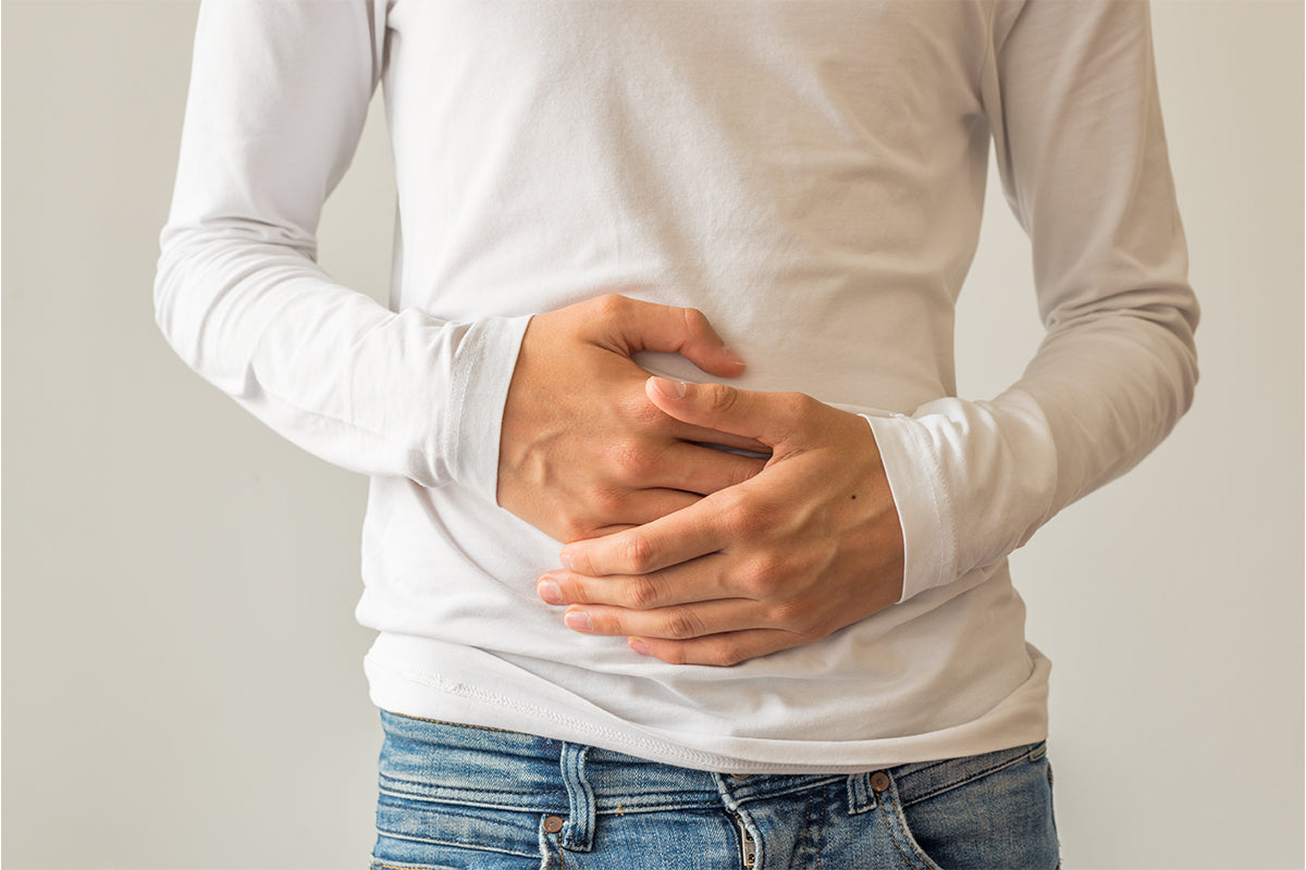 A person wearing a white long-sleeved shirt and jeans holds their stomach with both hands, indicating discomfort or pain.