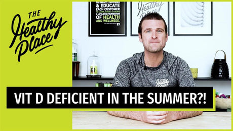 A man in a gray 'Find Your Healthy Place' shirt sits at a table with a wellness-themed background. Text overlay reads 'VIT D DEFICIENT IN THE SUMMER?!'