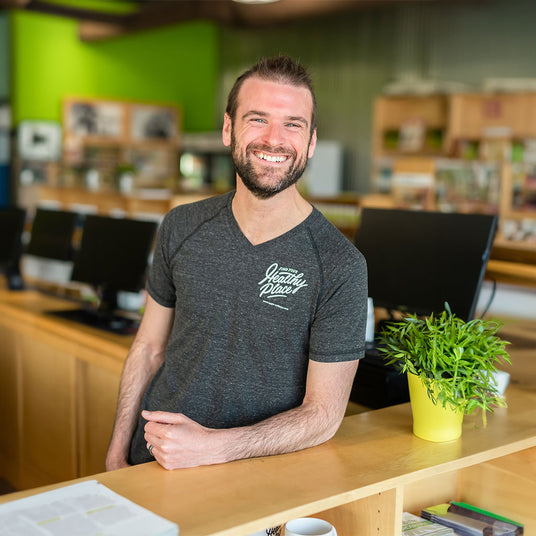 Tim OBrien owner of The Healthy Place smiling broadly in the Fitchburg store location. Shelves and green walls are blurred behind.