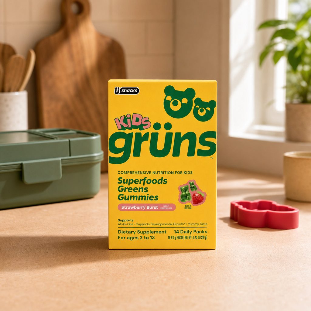 Grüns Kids Superfood Greens Gummies snack pack beside six strawberry gummy bears on a kitchen counter