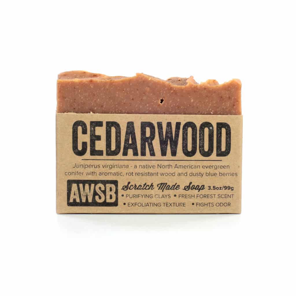 A natural bar of cedarwood soap, 3.5 ounces 99 grams, with a rustic brown label describing its purifying and exfoliating properties, featuring the text "AWSB Scratch Made Soap."