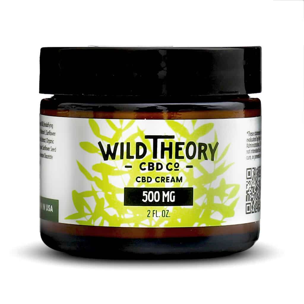 A small amber jar of Wild Theory CBD Co. CBD Cream, labeled as containing 500 mg of CBD in a 2 fl oz container. The label features green leafy graphics with bold black and green text and includes a QR code on the right side.