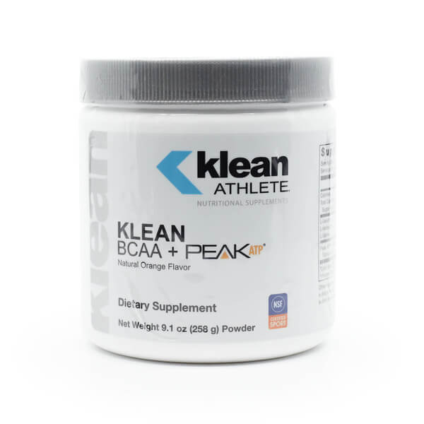 A white tub of Klean Athlete BCAA + Peak ATP powder with a silver lid and minimalist label design, featuring the NSF Certified for Sport logo. The supplement is flavored with natural orange, contains 30 servings, and has a net weight of 9.1 oz (258 g), designed to support energy and performance for athletes.
