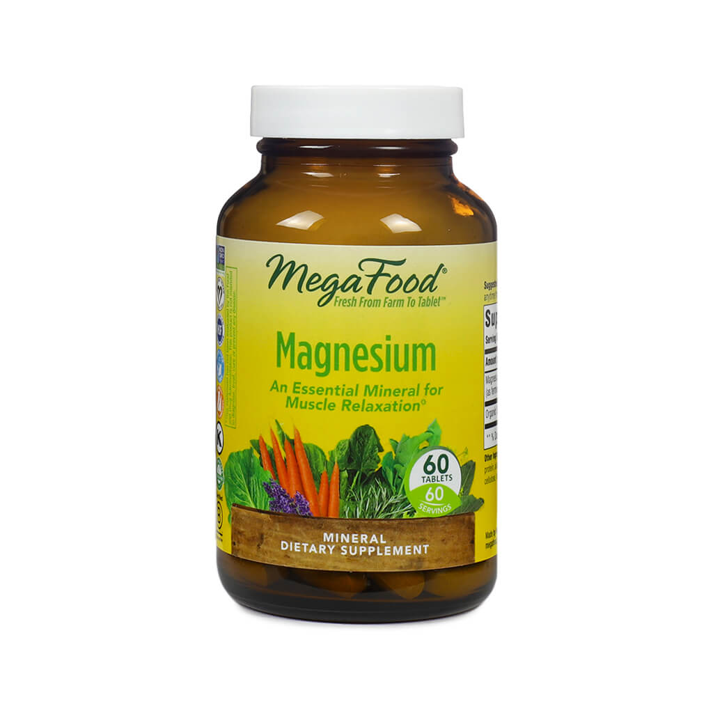 Amber bottle of MegaFood Magnesium supplement containing 60 tablets. The label is yellow and green with images of carrots, kale, and lavender, and text that reads "An Essential Mineral for Muscle Relaxation." The product is marketed as a mineral dietary supplement.