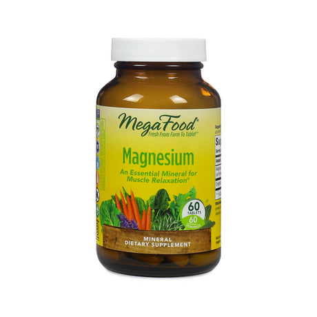 Amber bottle of MegaFood Magnesium supplement containing 60 tablets. The label is yellow and green with images of carrots, kale, and lavender, and text that reads "An Essential Mineral for Muscle Relaxation." The product is marketed as a mineral dietary supplement.