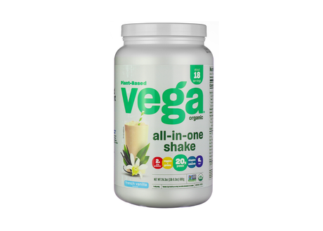 White container of Vega Organic All-in-One Shake in French vanilla flavor, with a vanilla smoothie, vanilla flower, and green leaves on the label. The front highlights plant-based ingredients, 20g of protein, 2 servings of veggies and greens, 6g of fiber, added vitamins and minerals, and displays USDA Organic and Non-GMO Project Verified certifications.