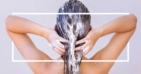 A woman massages shampoo or conditioner into her wet hair, with a white rectangular border framing the image.