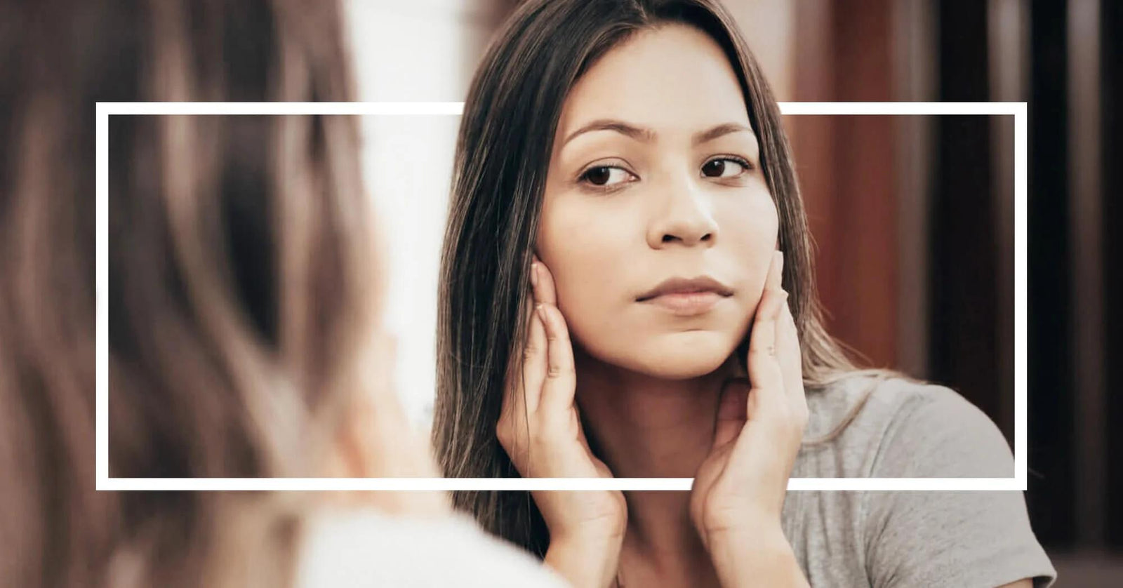 A woman touches her cheeks while examining her skin in the mirror.