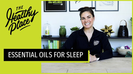 A video thumbnail from "The Healthy Place" featuring a smiling woman at a table with bold text reading "ESSENTIAL OILS FOR SLEEP" and the brand’s logo on a lime green background.