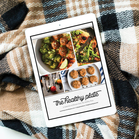 The Healthy Plate cookbook on a tablet, featuring images of healthy recipes like broccoli dishes and desserts, styled against a checkered blanket for a cozy presentation.