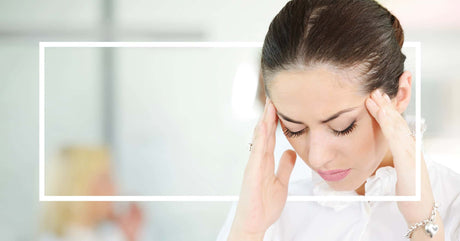 A woman in a white blouse presses her temples with a pained expression, framed by a white rectangular border.