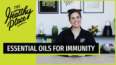 Smiling woman in a 'Find Your Healthy Place' jacket sits at a table with a wellness-themed background. Bold text overlay reads 'ESSENTIAL OILS FOR STRESS.'
