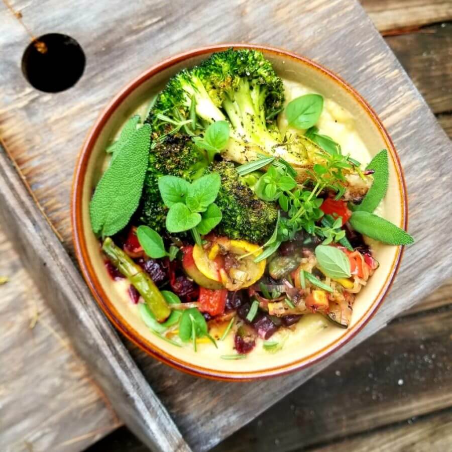 A bowl filled with a variety of colorful plant-based foods rich in protein, including roasted broccoli, mixed grilled vegetables, and fresh herbs, all served on a rustic wooden table, showcasing a nutritious and protein-packed vegan meal option.