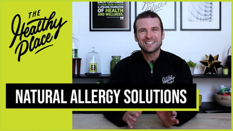 A man in a black 'Find Your Healthy Place' jacket sits at a table with a wellness-themed background. Text overlay reads 'NATURAL ALLERGY SOLUTIONS.'