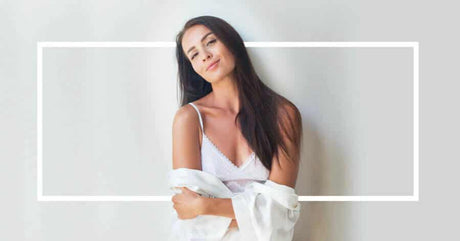 A confident woman in a white lace camisole poses against a neutral background.