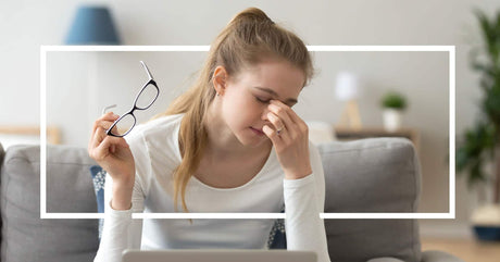 A tired young woman sits on a couch, holding her glasses and pinching her nose in fatigue, with a laptop open in front of her.