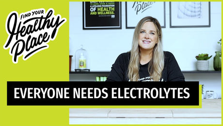 A woman in a 'Find Your Healthy Place' sweatshirt sits at a table with a wellness-themed background. Text overlay reads 'EVERYONE NEEDS ELECTROLYTES.'