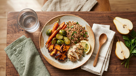 A balanced wholesome meal of roasted carrots, brussels sprouts, farro, and herbed chicken on a wooden table.
