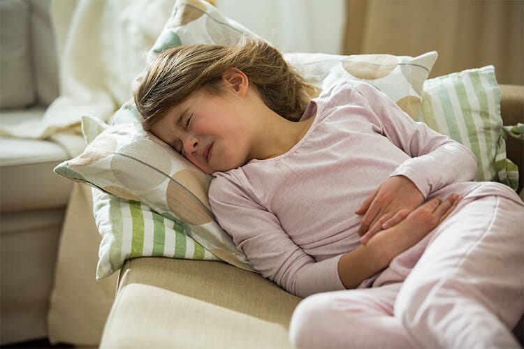 A young girl sleeping on a couch, clutching her stomach in discomfort, suggesting she may be unwell.