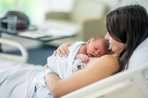 A new Mother holds her baby gently to her chest as they spend time bonding with some skin-to-skin time. She is wearing hospital gown and the baby is swaddled loosely as Mom and baby spend time together shortly after delivery.