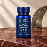 Life Extension Aged Black Garlic bottle on a red marble surface beside a curved smoked-glass arch