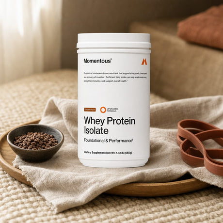 Momentous Whey Protein Isolate Chocolate tub beside a prepared chocolate shake
