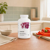 Thorne Women's Multi 50+ bottle with capsules and water glass on a counter
