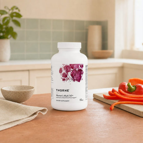 Thorne Women's Multi 50+ bottle with capsules and water glass on a counter