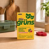 Grüns Kids Superfood Greens Gummies snack pack beside six strawberry gummy bears on a kitchen counter