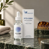 InfiniWell PTD-DBM scalp serum dropper bottle and box on a marble counter beside a comb and towel
