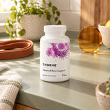 Thorne Advanced Bone Support bottle on a green kitchen counter with a potted plant and a resistance band