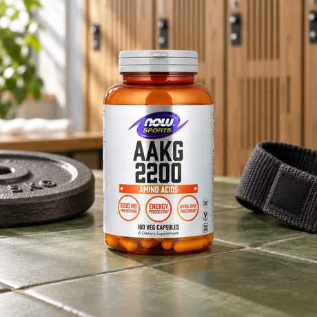 NOW Sports AAKG 2200 bottle on a tiled floor beside a weight plate and a resistance band, lockers behind
