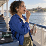 Chuga Pure Himalayan Shilajit Tablets box on a ferry bench while a woman takes a tablet, steel water bottle in hand