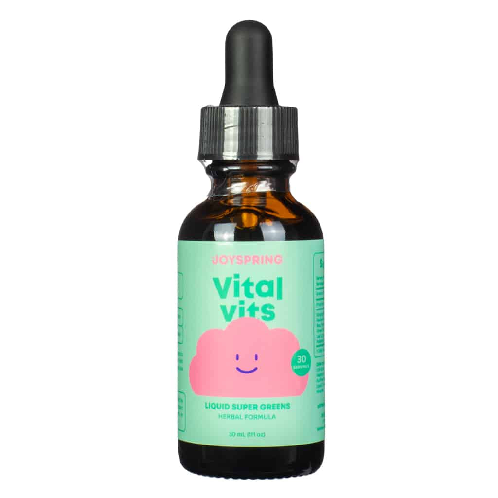 A 1 fl. oz (30 mL) amber dropper bottle of JoySpring Vital Vits, with a pastel green label and a smiling pink cloud icon. The label highlights 30 servings of a liquid super greens herbal formula, designed to provide daily multivitamin support for kids.
