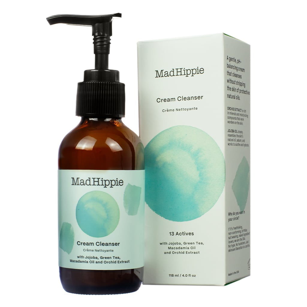 A 4 oz / 118 ml bottle of Mad Hippie Cream Cleanser with a pump, placed next to its box featuring a teal watercolor design. The cleanser contains 13 actives, including jojoba, green tea, macadamia oil, and orchid extract, designed for gentle, pH-balanced cleansing without stripping natural oils."