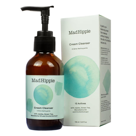 A 4 oz / 118 ml bottle of Mad Hippie Cream Cleanser with a pump, placed next to its box featuring a teal watercolor design. The cleanser contains 13 actives, including jojoba, green tea, macadamia oil, and orchid extract, designed for gentle, pH-balanced cleansing without stripping natural oils."