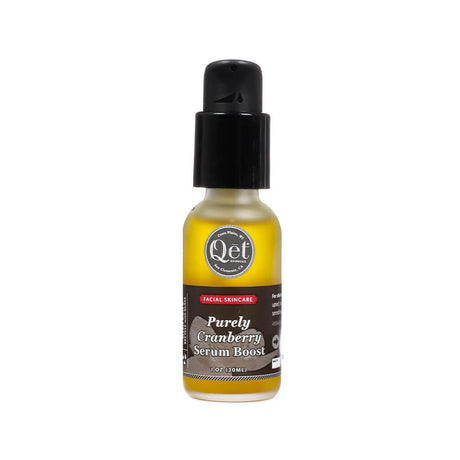 A 1 oz frosted glass bottle of Qēt Botanicals Purely Cranberry Serum Boost with a black pump top and a rich yellow tint to the serum. The label designates it as a facial skincare product aimed at delivering antioxidant-rich hydration for radiant skin. 