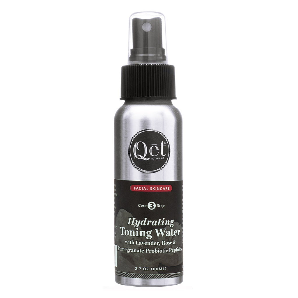 A silver spray bottle of Qēt Botanicals Hydrating Toning Water with Lavender, Rose, Pomegranate, and Probiotic Peptides. The black label displays the Qēt Botanicals logo, with the product name in white text below. A red banner at the top indicates it's part of the Facial Skincare line, labeled as Step 3 in a skincare routine. The bottle has a black spray nozzle with a clear cap, and the volume is listed as 2.7 oz (80ml).