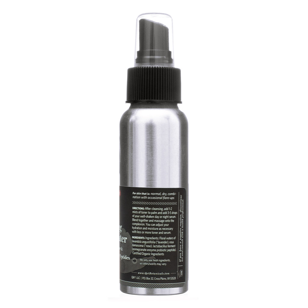 Back of a silver spray bottle with a black pump, displaying product directions and ingredients. The label suggests using the toner with serums for added hydration and mentions ingredients like floral waters, rose damascena extract, and probiotic peptides. Designed for normal, dry, and combination skin with occasional flare-ups.