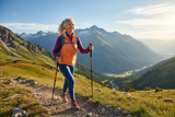 An aging woman in exercise clothing on a hike with hiking poles on a mountain, sunny, beautiful. She's feeling vibrant and happy and full of energy.