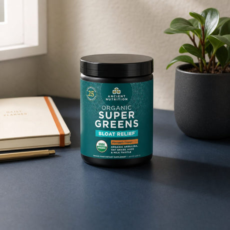 Ancient Nutrition Organic SuperGreens Bloat Relief Pineapple Orange tub beside a prepared greens drink