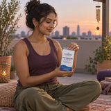 Nordic Naturals Magnesium Complex box held by a woman sitting cross-legged on a rooftop at sunset